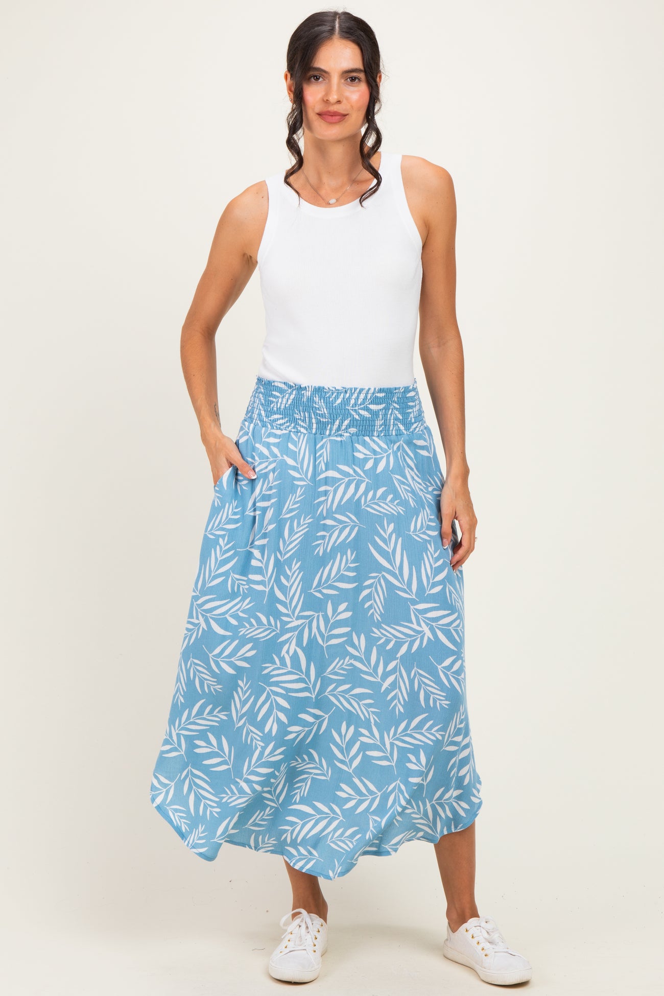 woman wearing a white tank top and a blue floral print maxi skirt with an elastic waistband and pockets