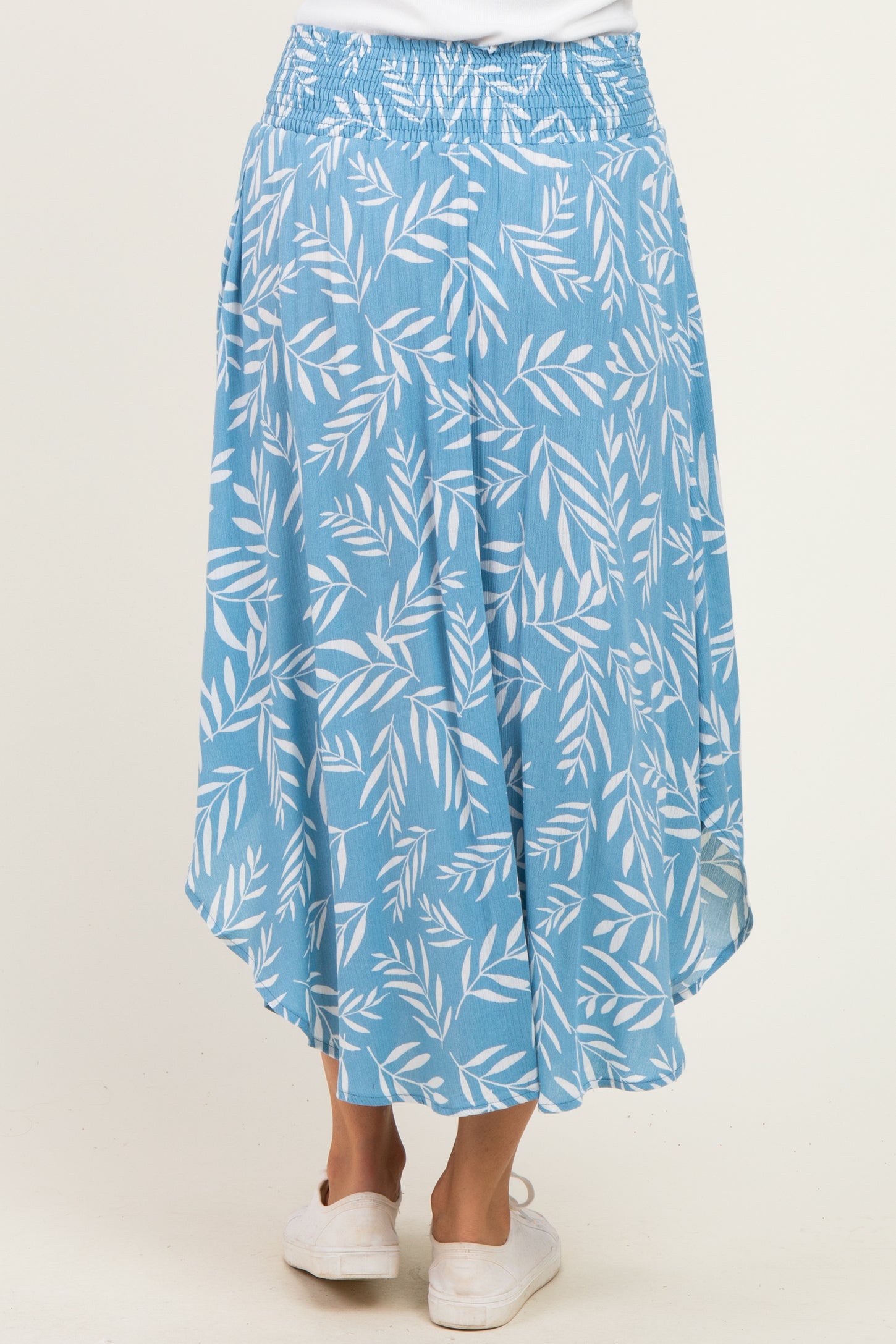 woman wearing a light blue skirt with a leaf print and an asymmetrical hemline, showing the back view