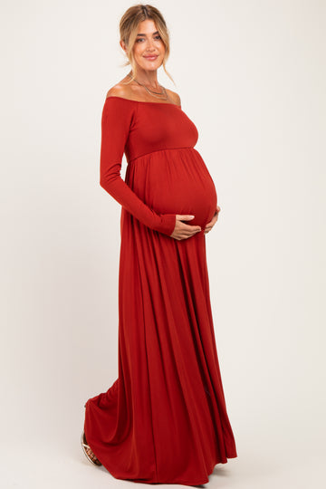woman wearing a rust red off-shoulder maternity maxi dress with a visible baby bump