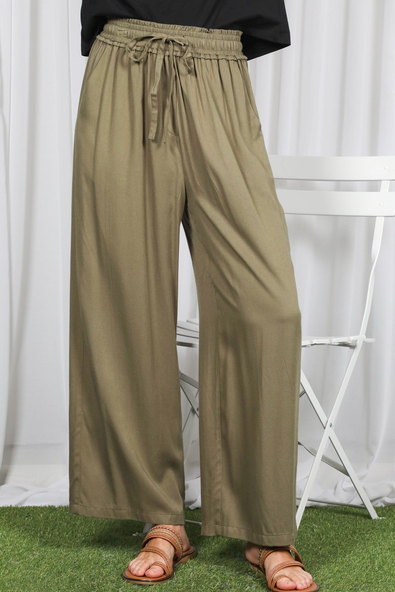 woman wearing olive green wide-leg pants with an elastic waistband and drawstring, standing on grass