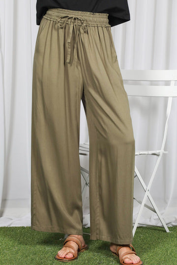 woman wearing olive green wide-leg pants with an elastic waistband and drawstring, standing on grass