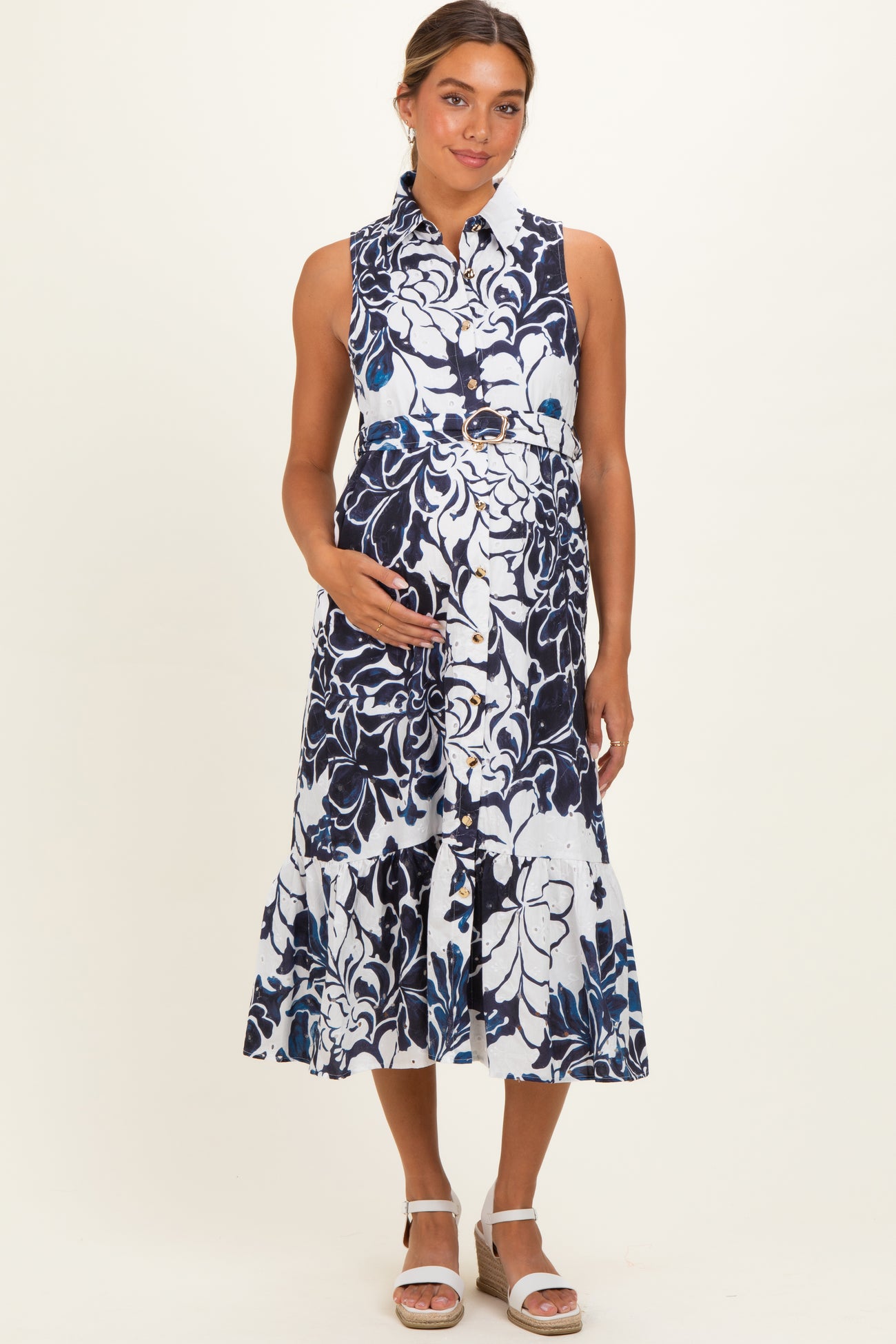 woman wearing a navy and white floral maternity dress with a button front and ruffle hem, holding her baby bump