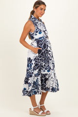 woman wearing a floral print sleeveless maternity dress with a ruffled hem and pockets, showing her baby bump