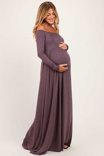 woman wearing a mauve off-the-shoulder long sleeve maternity dress and cradling her baby bump