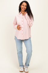 woman wearing a pink and white striped maternity button-up shirt and light blue jeans, cradling her baby bump