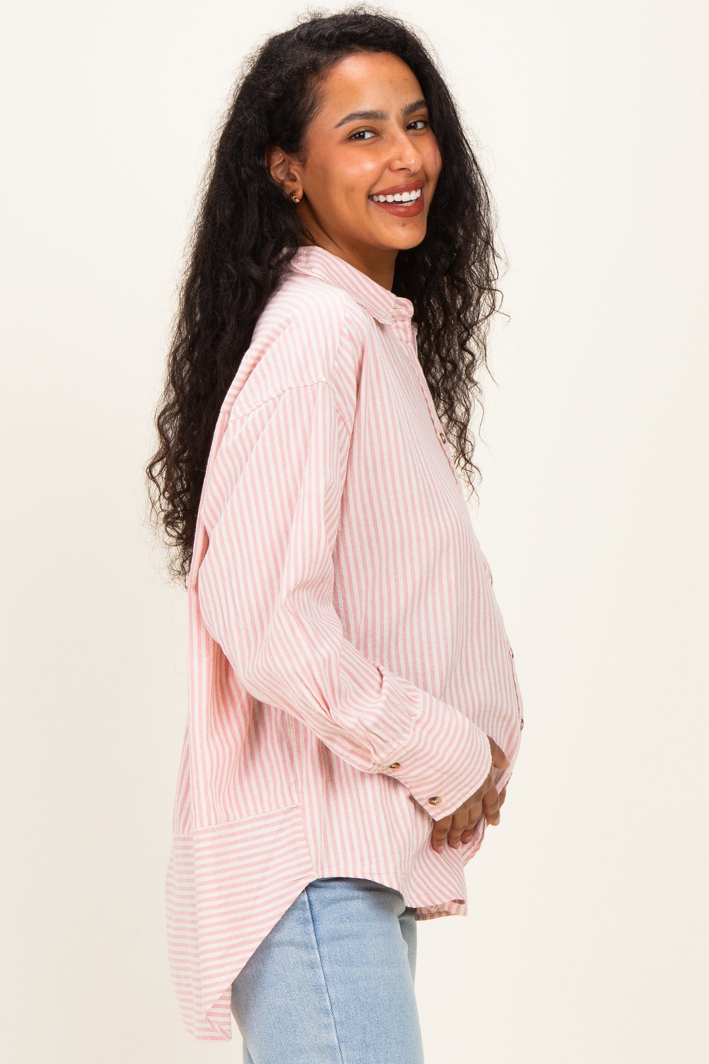 woman wearing a light pink and white striped maternity button-up shirt, showing her baby bump