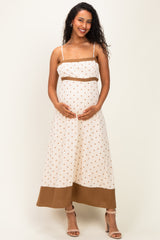 woman wearing a cream maternity maxi dress with brown polka dots and color block hem, holding her baby bump
