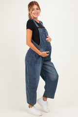 woman wearing a dark blue denim maternity overall, holding her baby bump with a black t-shirt underneath