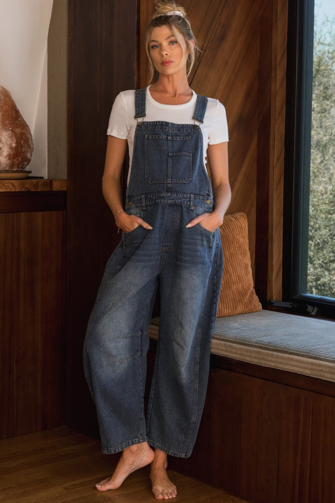 woman wearing a blue denim maternity overall with a white t-shirt, standing indoors with relaxed fit and pockets