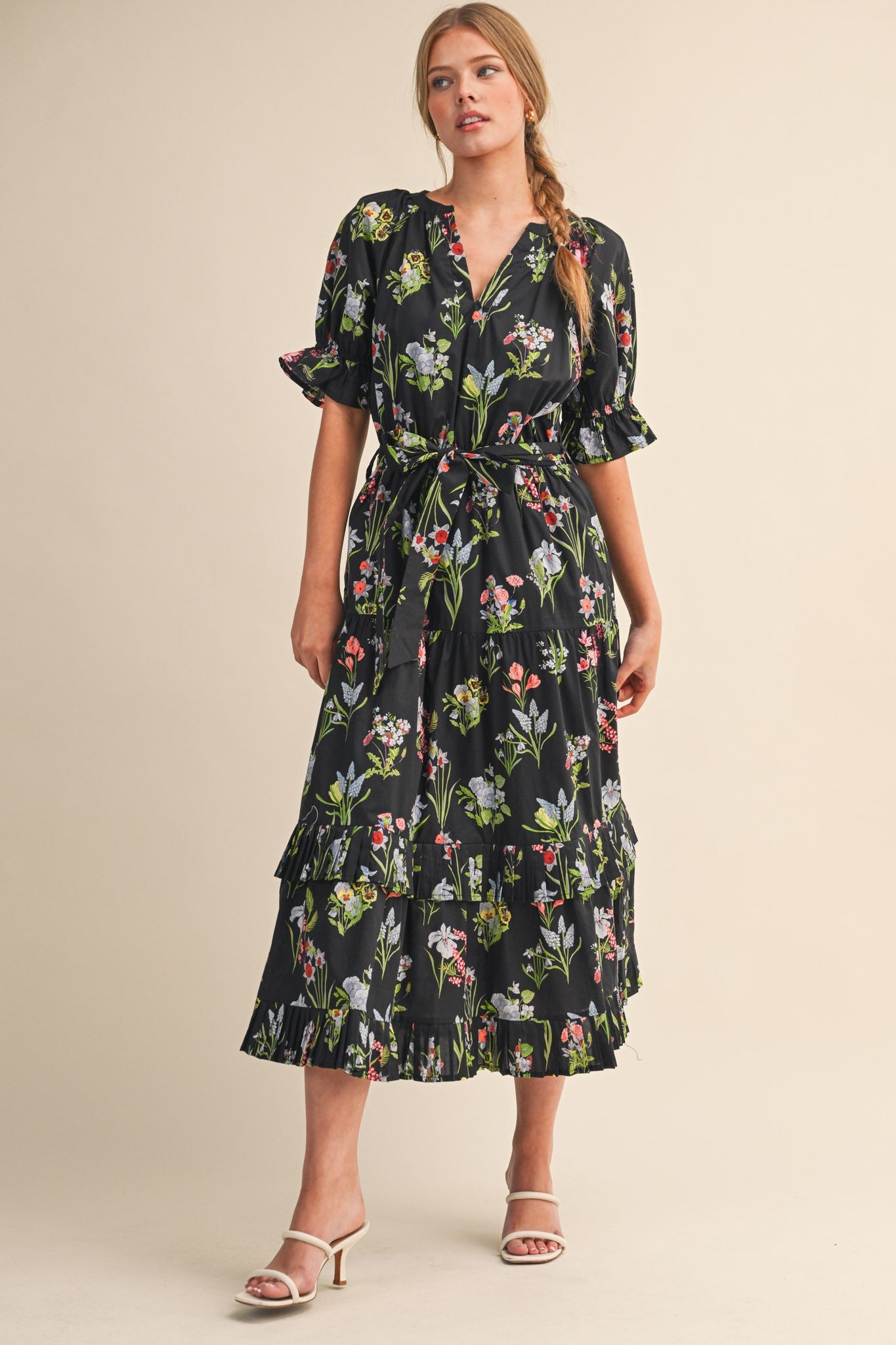 woman wearing a black floral maxi dress with ruffled sleeves and a tie waist, standing in a neutral background