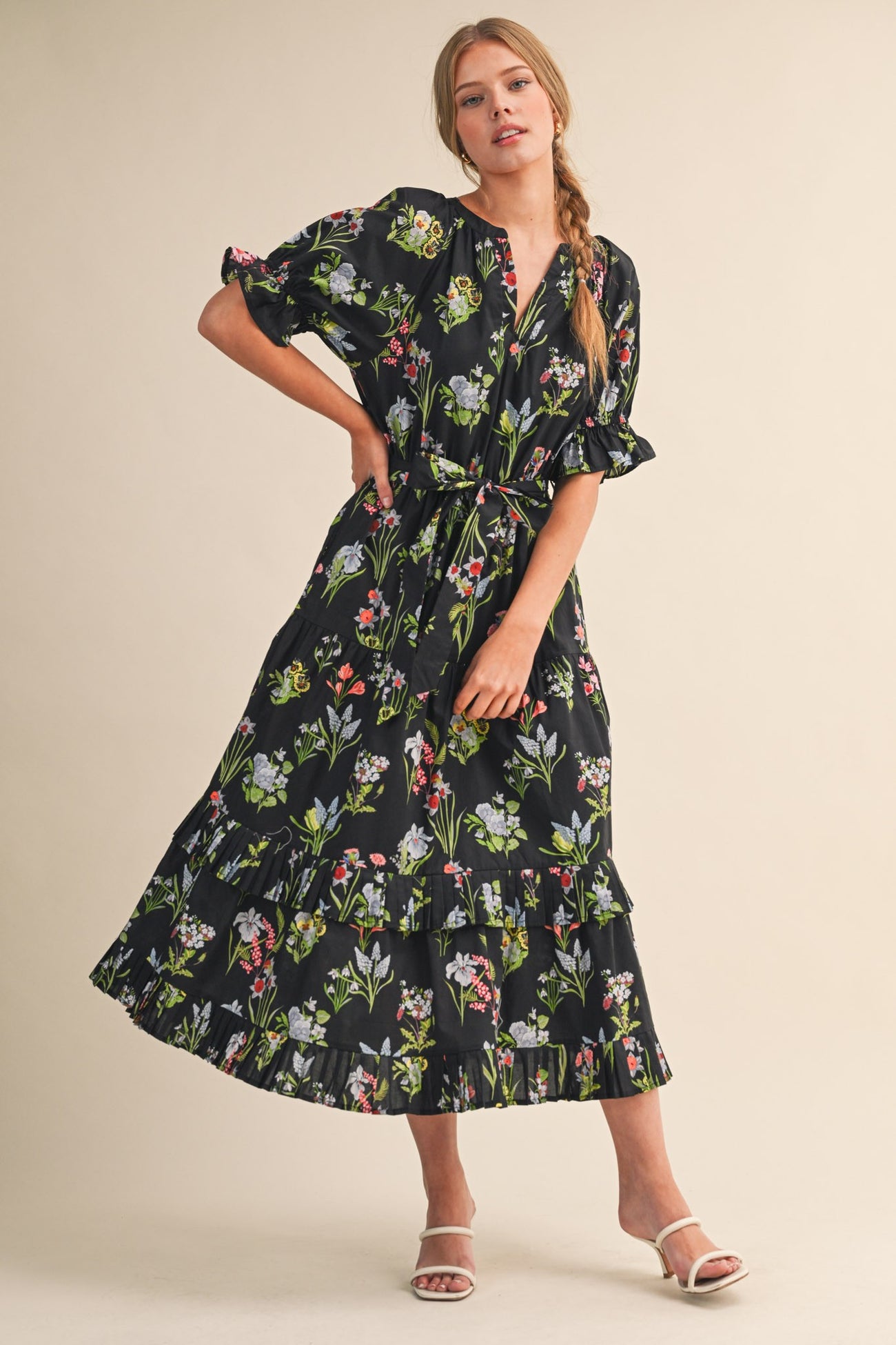 woman wearing a black floral maxi dress with short sleeves and a tiered skirt, posing with a hand on her hip