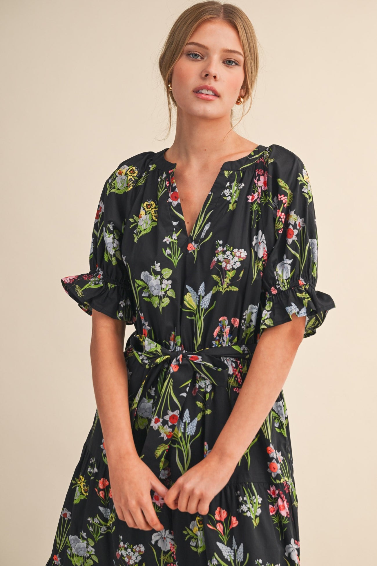 woman wearing a black floral midi dress with short puff sleeves and a tie waist detail