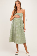 woman wearing a green and white gingham maternity dress with adjustable straps and holding her baby bump