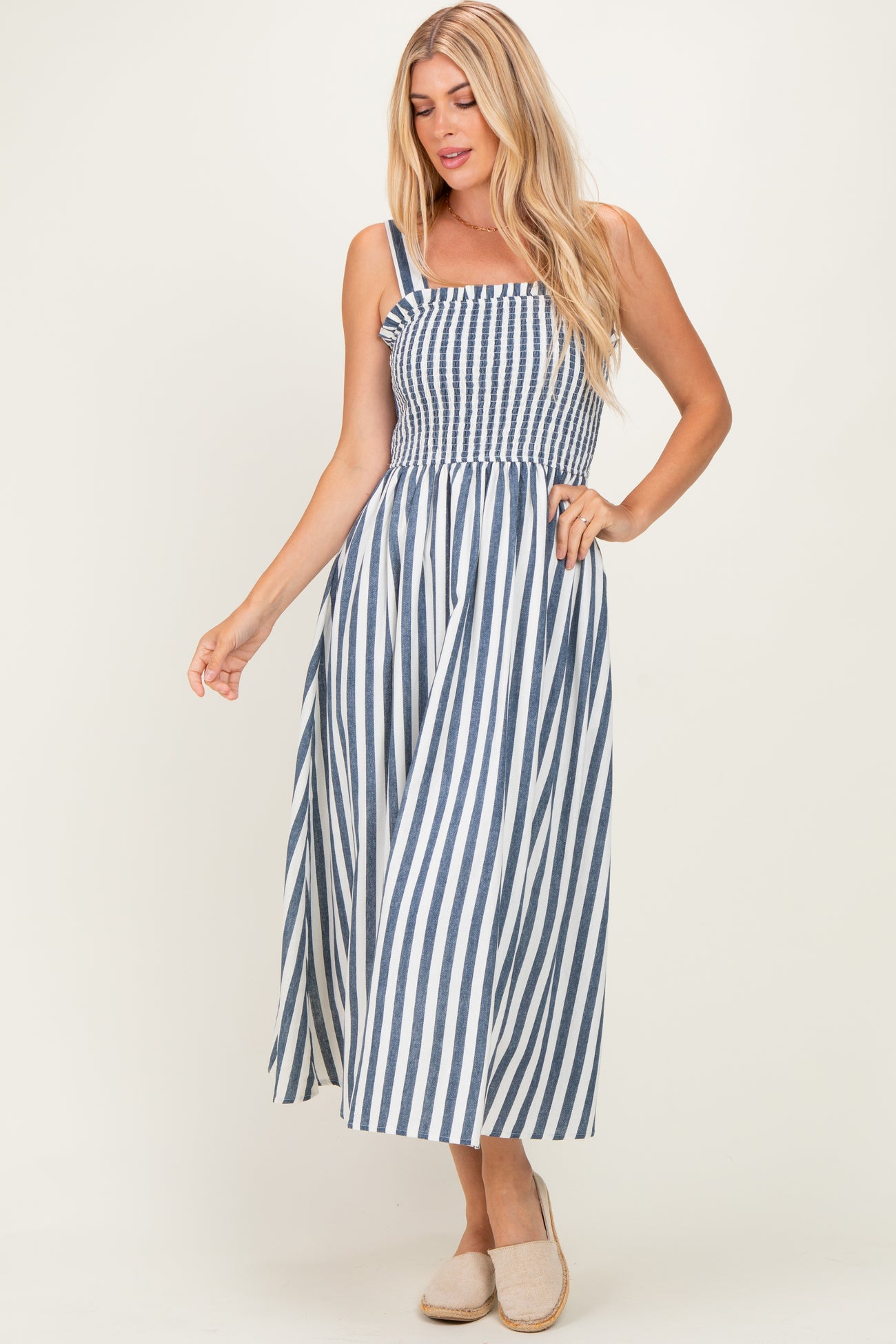 woman wearing a blue and white striped sleeveless maxi dress with a smocked bodice and ruffled detail