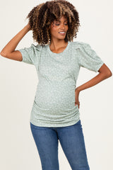 woman wearing a green floral maternity top with puff sleeves and a visible baby bump