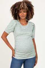 woman wearing a green floral maternity top with puff sleeves and a visible baby bump, paired with blue jeans