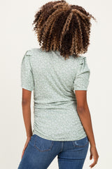 woman wearing a light green floral maternity top with puff sleeves and ruched sides, showing her baby bump from the back