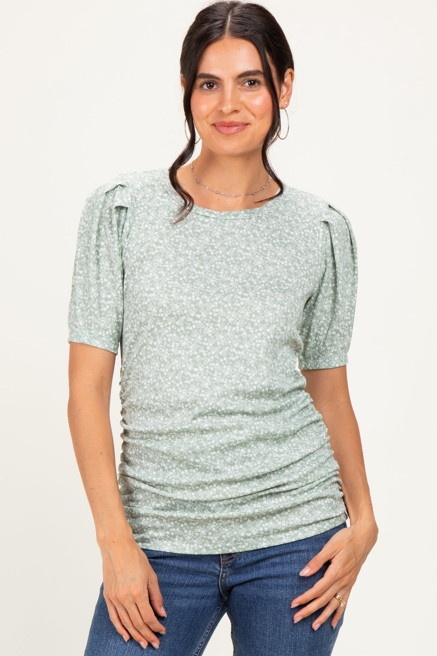 woman wearing a green floral short sleeve top with puff sleeves and ruched detailing, paired with denim jeans