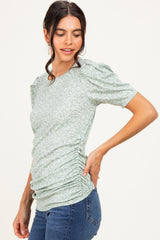 woman wearing a green floral short sleeve top with ruched sides and a fitted silhouette, paired with denim jeans