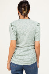 woman wearing a green floral short sleeve top with ruched sides and puff sleeves, shown from the back