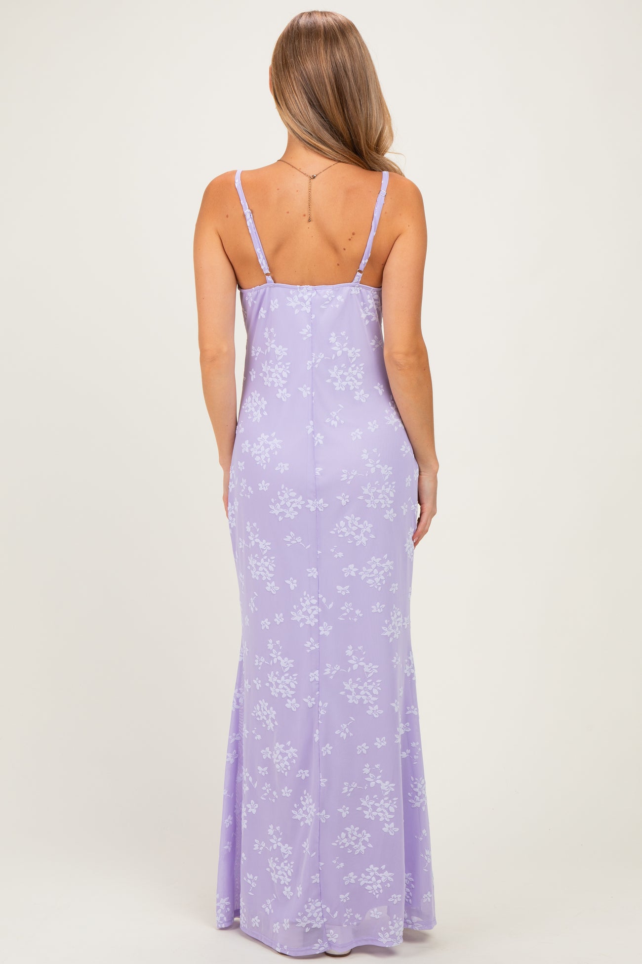 woman wearing a lavender maxi dress with a floral print and thin straps, shown from the back