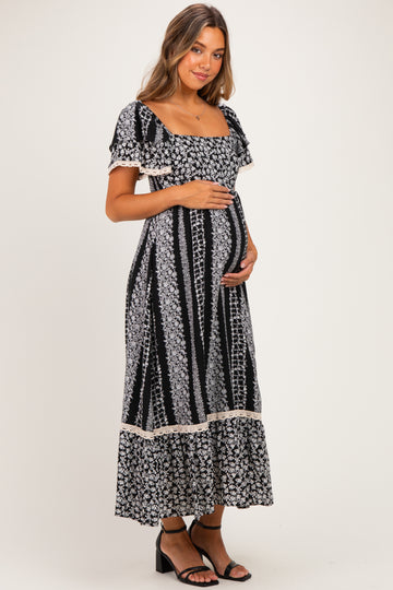 woman wearing a black floral print maternity dress with short sleeves and a square neckline, holding her baby bump