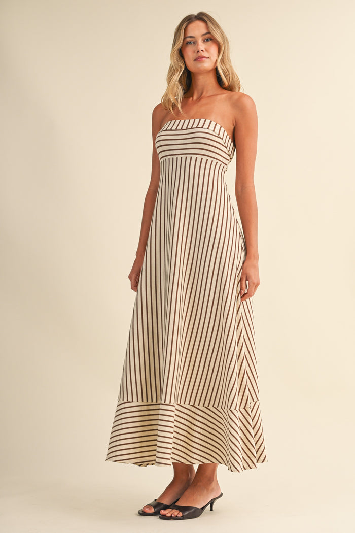 woman wearing a strapless beige maxi dress with vertical brown stripes and a flared hem, standing against a light background