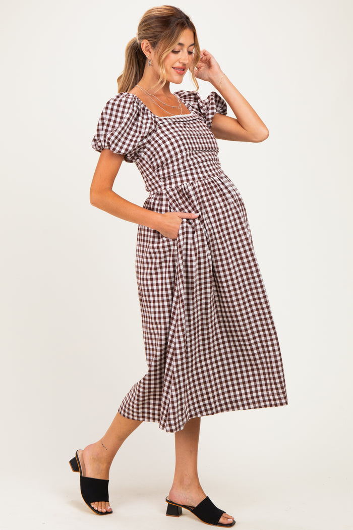 woman wearing a brown and white checked maternity dress with puff sleeves and pockets, showing her baby bump