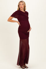 woman wearing a burgundy ruched maternity gown with a sheer skirt and a baby bump visible