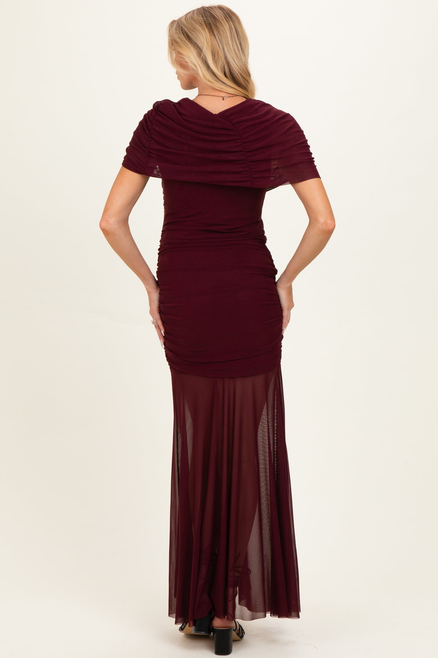 woman wearing a burgundy maternity gown with ruched bodice and sheer maxi skirt, showing a baby bump from the back