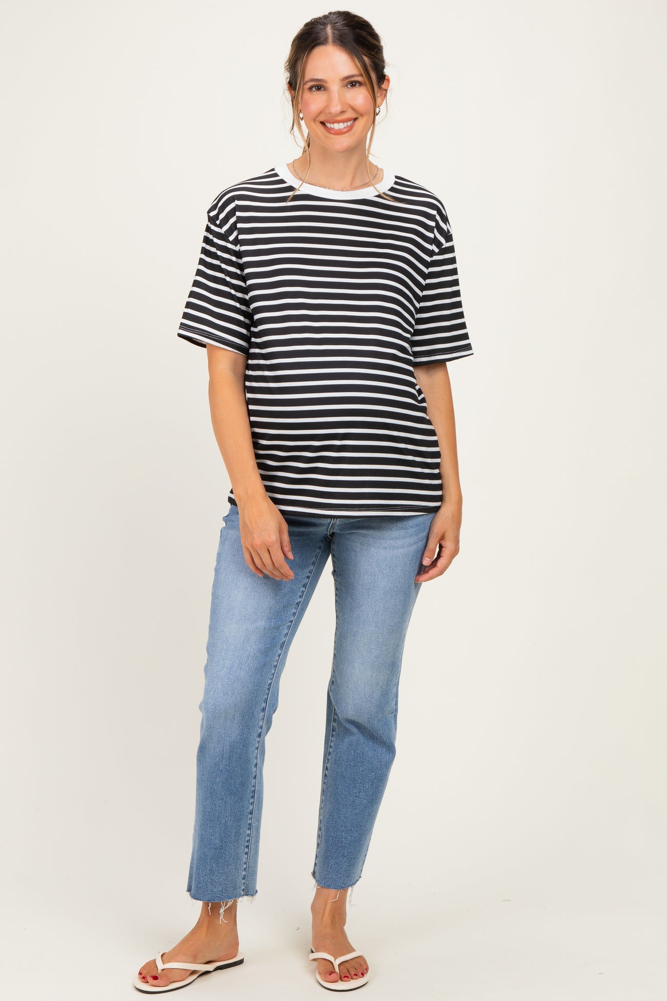 woman wearing a black and white striped maternity top with short sleeves and blue jeans, showing a baby bump