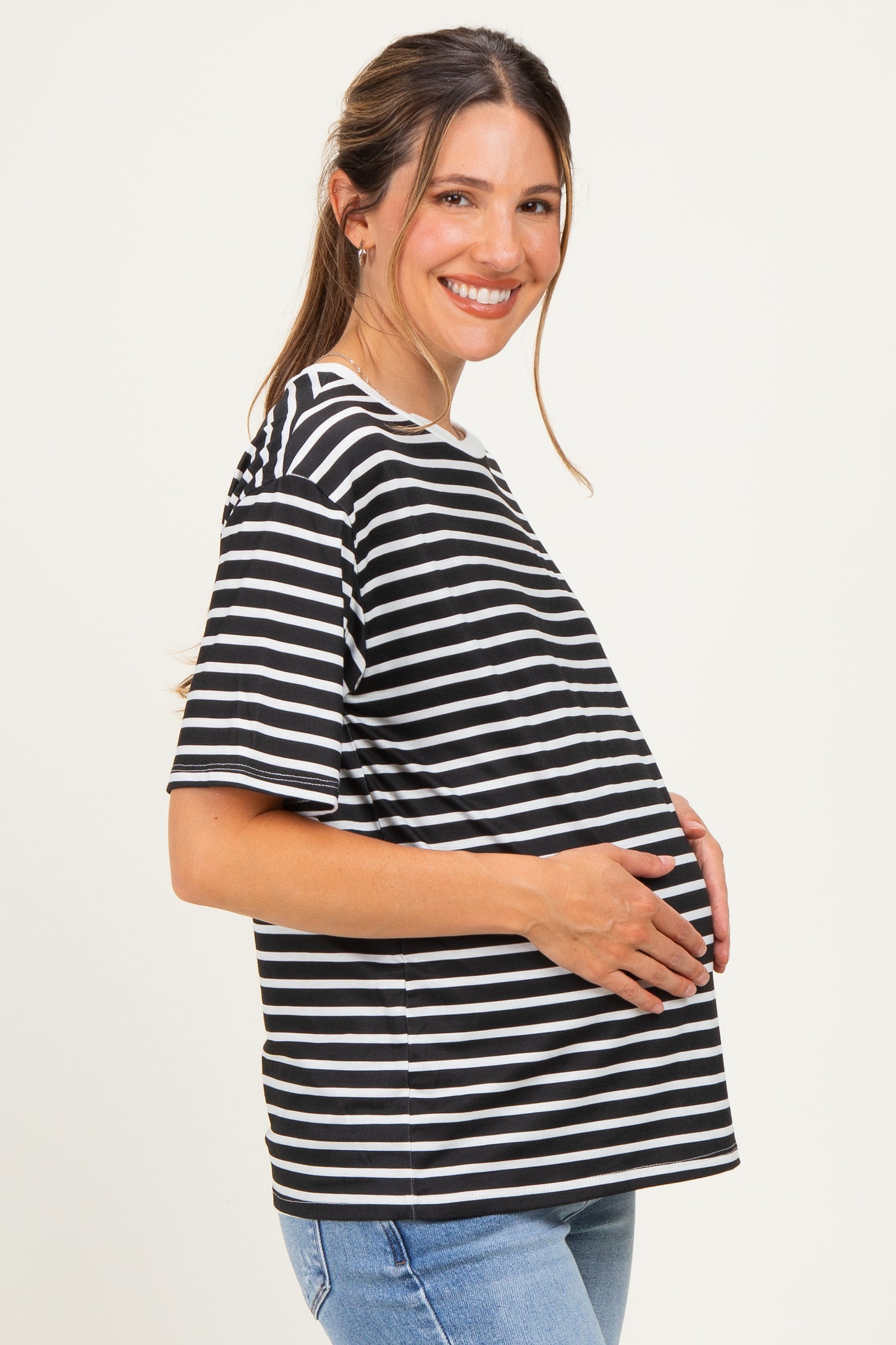 woman wearing a black and white striped maternity top and holding her baby bump