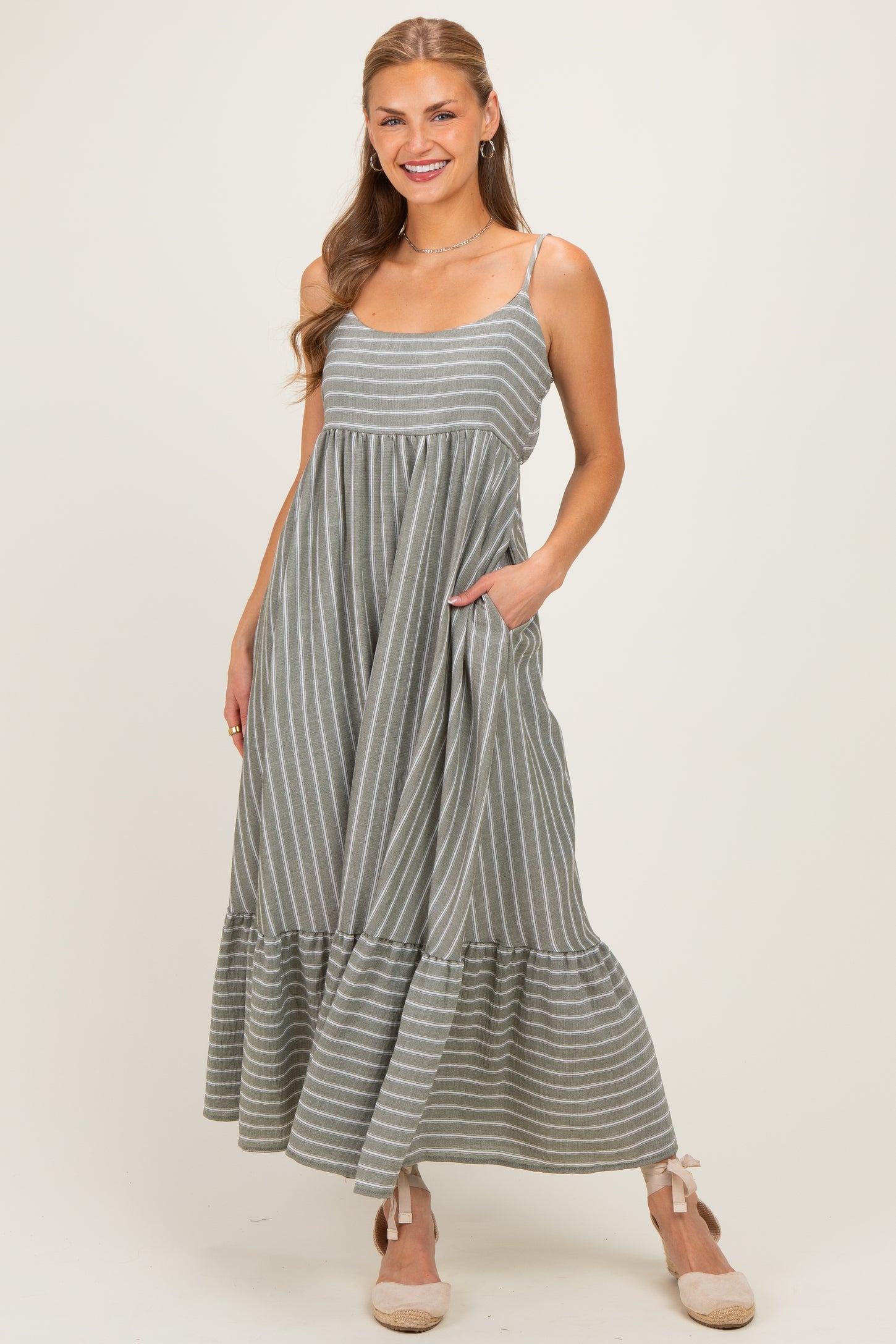 woman wearing a grey striped maxi dress with a ruffled hem and pockets, smiling at the camera