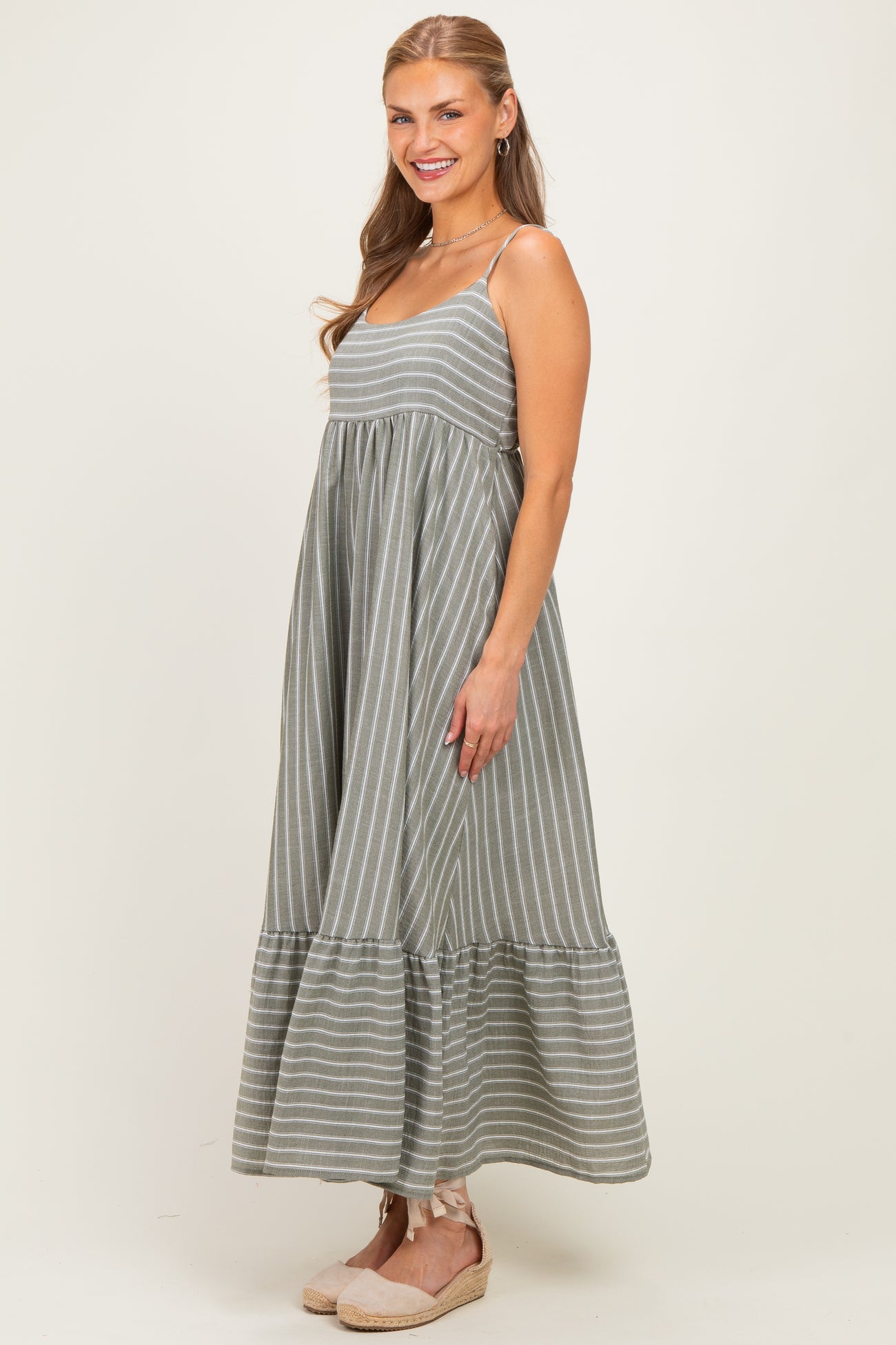 woman wearing a gray striped maxi dress with a tiered hem and thin straps, posed in a light-filled setting