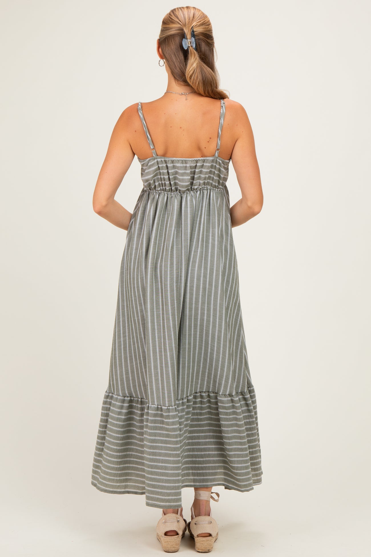 woman wearing a gray and white striped maxi dress with adjustable spaghetti straps and a ruffled hemline