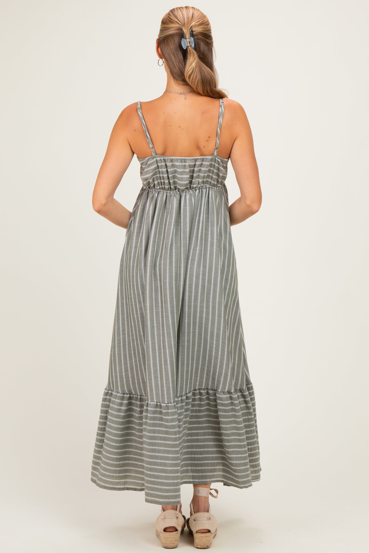 woman wearing a gray and white striped maxi dress with adjustable spaghetti straps and a ruffled hemline
