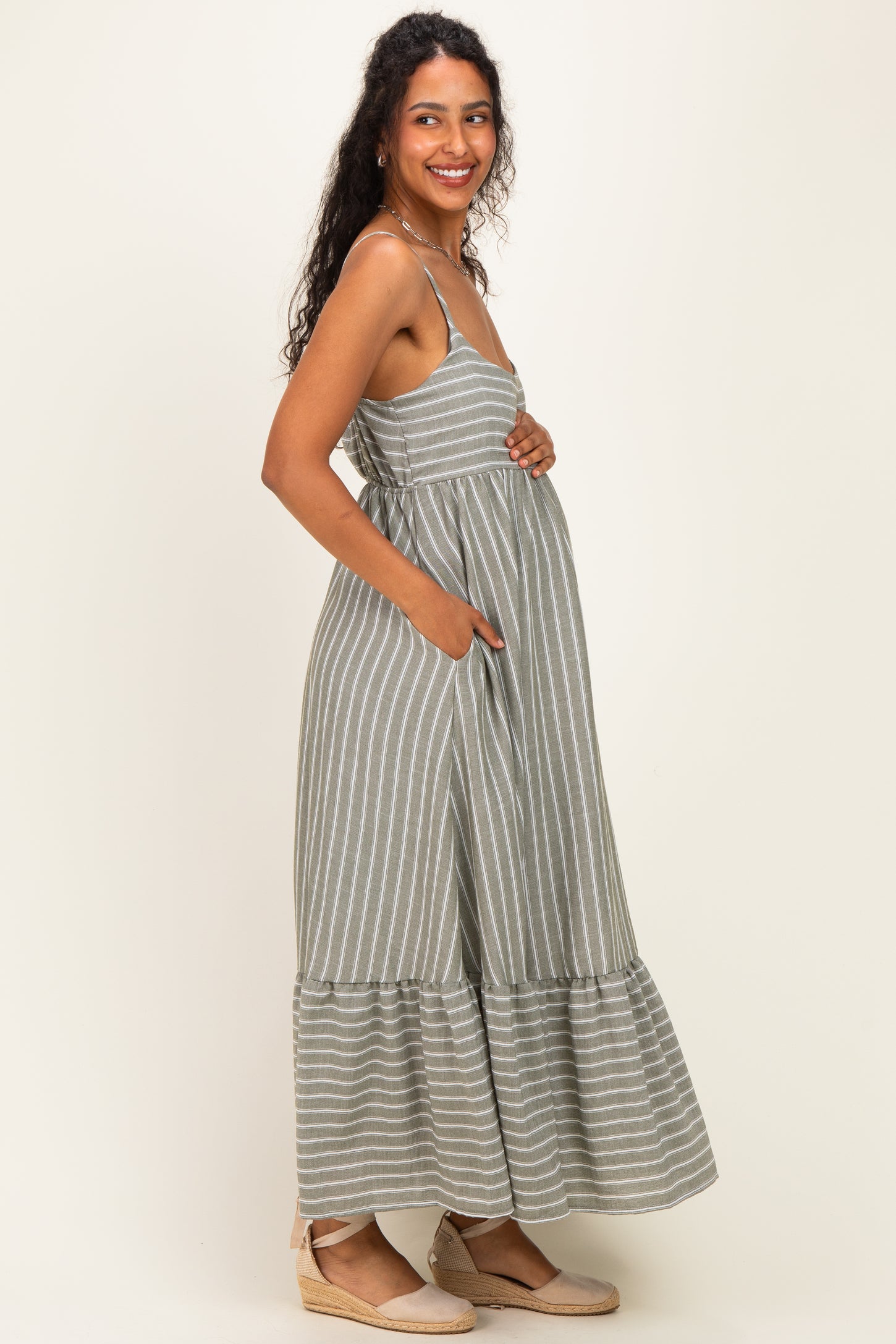 woman wearing a green and white striped maternity maxi dress with pockets and a visible baby bump