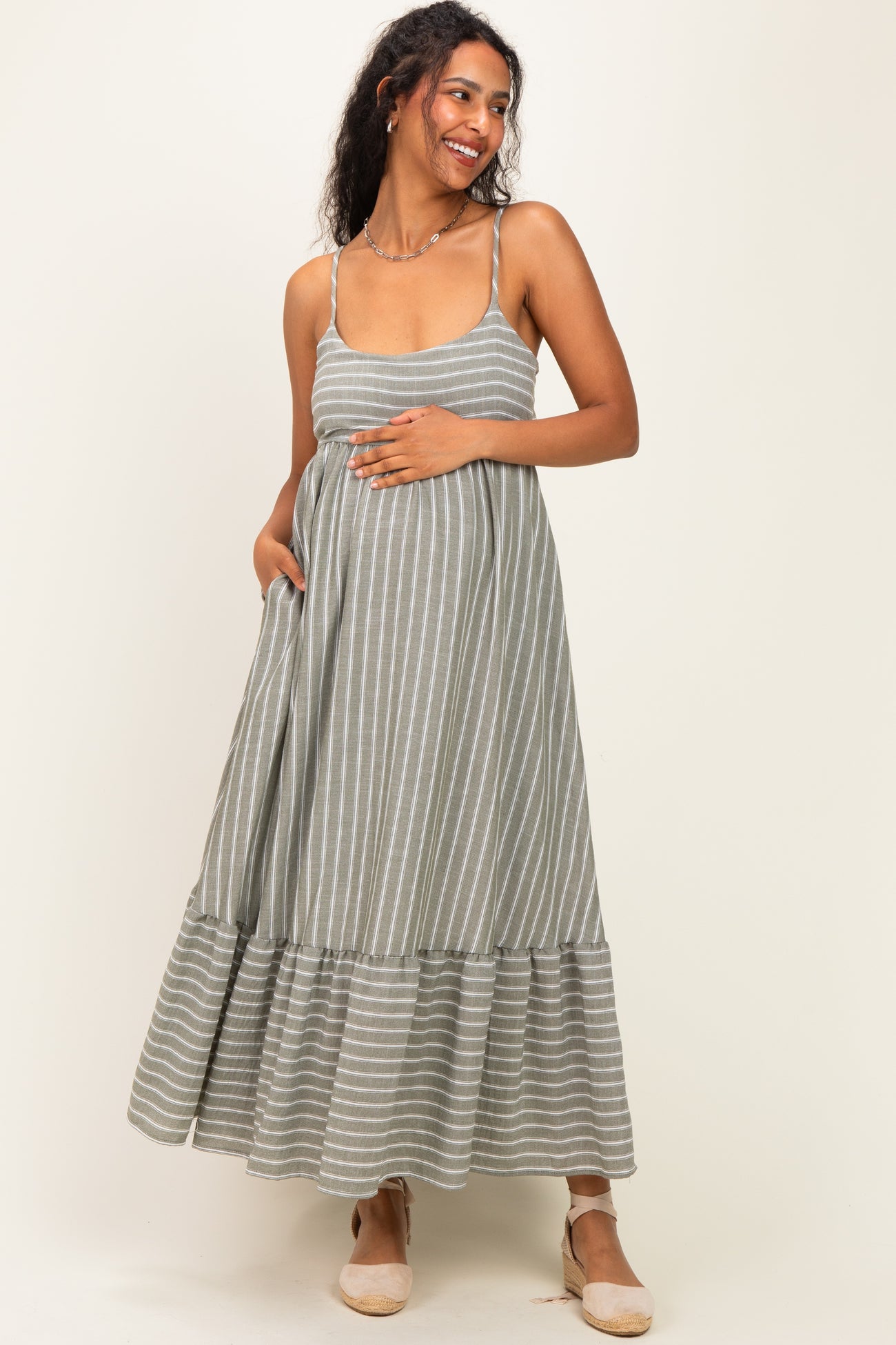 woman wearing a gray striped maternity maxi dress with a ruffled hem and holding her baby bump