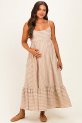 woman wearing a beige striped maternity maxi dress with a tiered hem and holding her baby bump