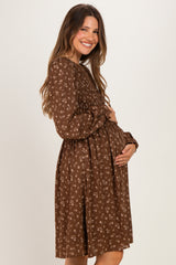 woman wearing a brown floral maternity dress with long sleeves and holding her baby bump