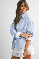 woman wearing a blue striped oversized button-up shirt with rolled sleeves and a white ruffled mini skirt