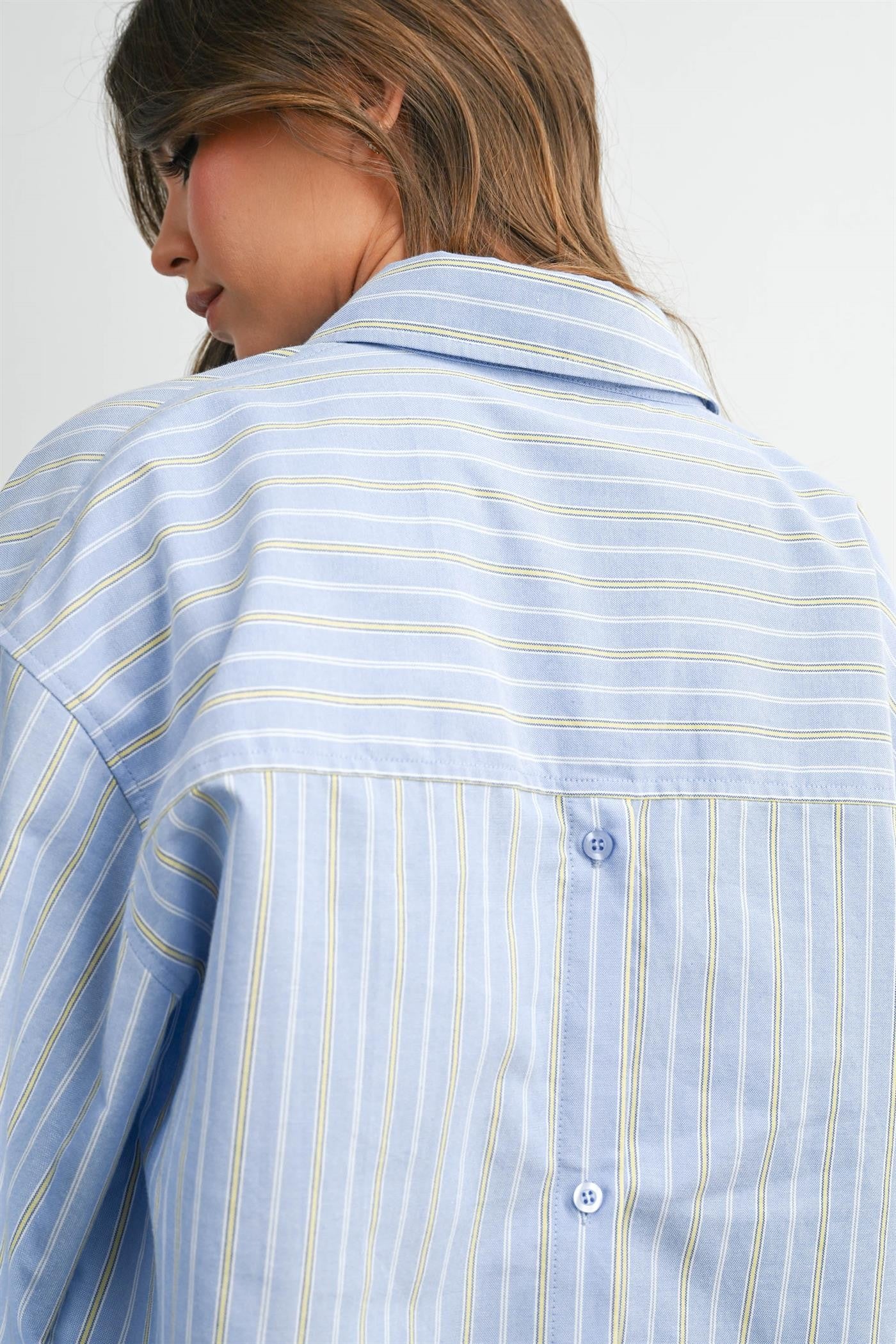 woman wearing a light blue striped button-up shirt, showcasing the back detail and collar style