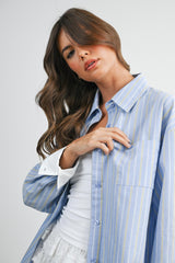woman wearing a light blue striped oversized shirt with a chest pocket and a white tank top underneath