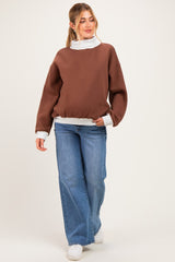 woman wearing a brown oversized maternity sweatshirt with a white collar and cuffs, paired with wide-leg jeans