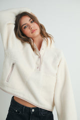woman wearing a cream cropped fleece pullover with a half-zip and front pocket, styled with black jeans