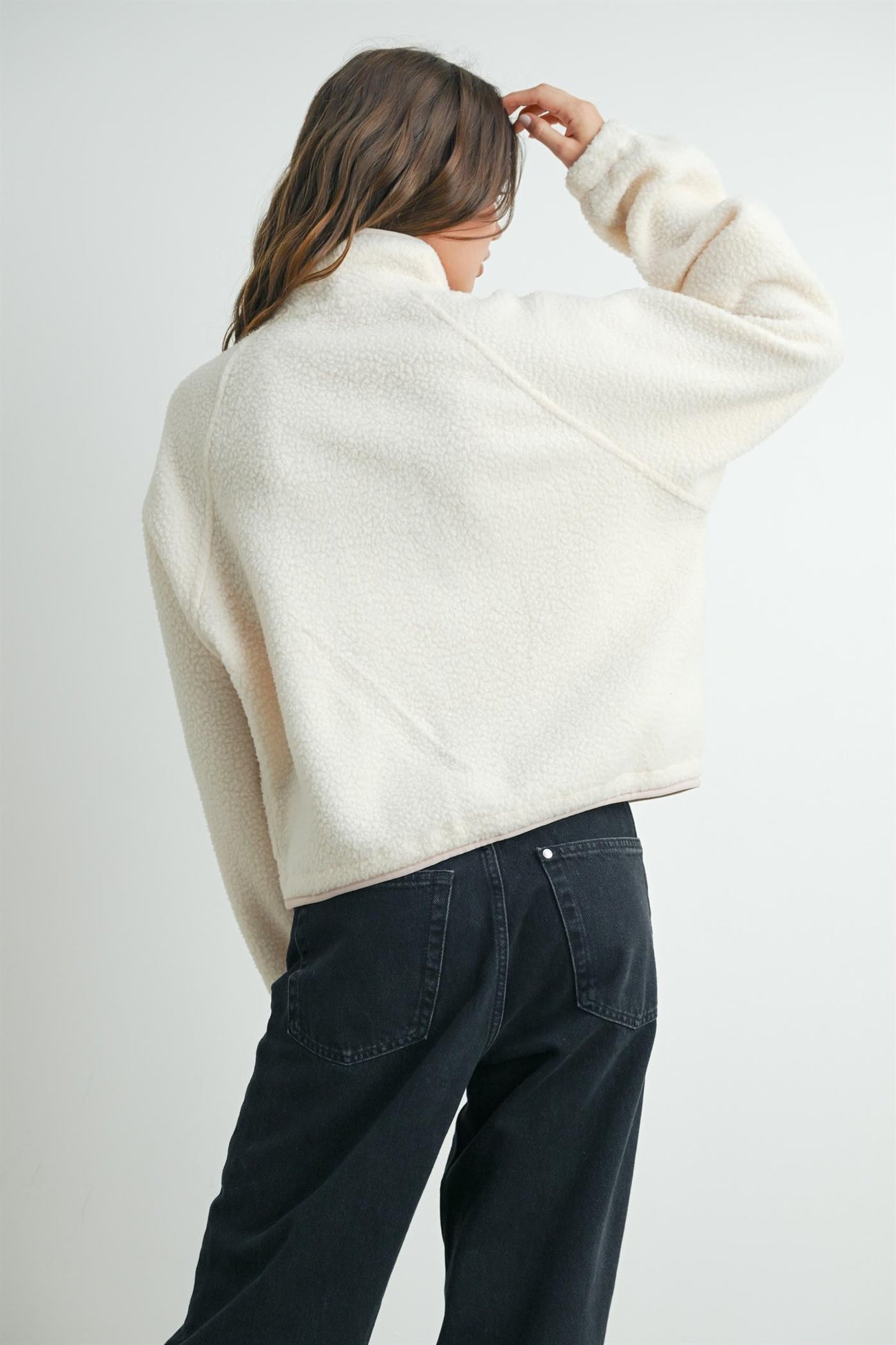 woman wearing a cream-colored fleece pullover with a high collar and back view, paired with black jeans
