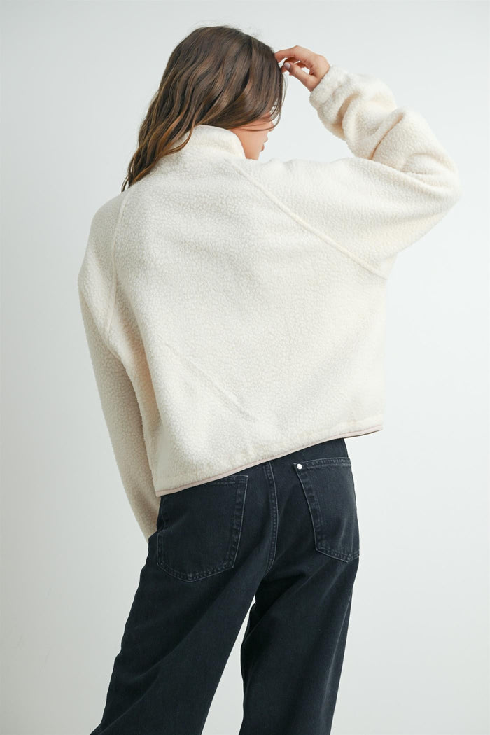 woman wearing a cream-colored fleece pullover with a high collar and back view, paired with black jeans
