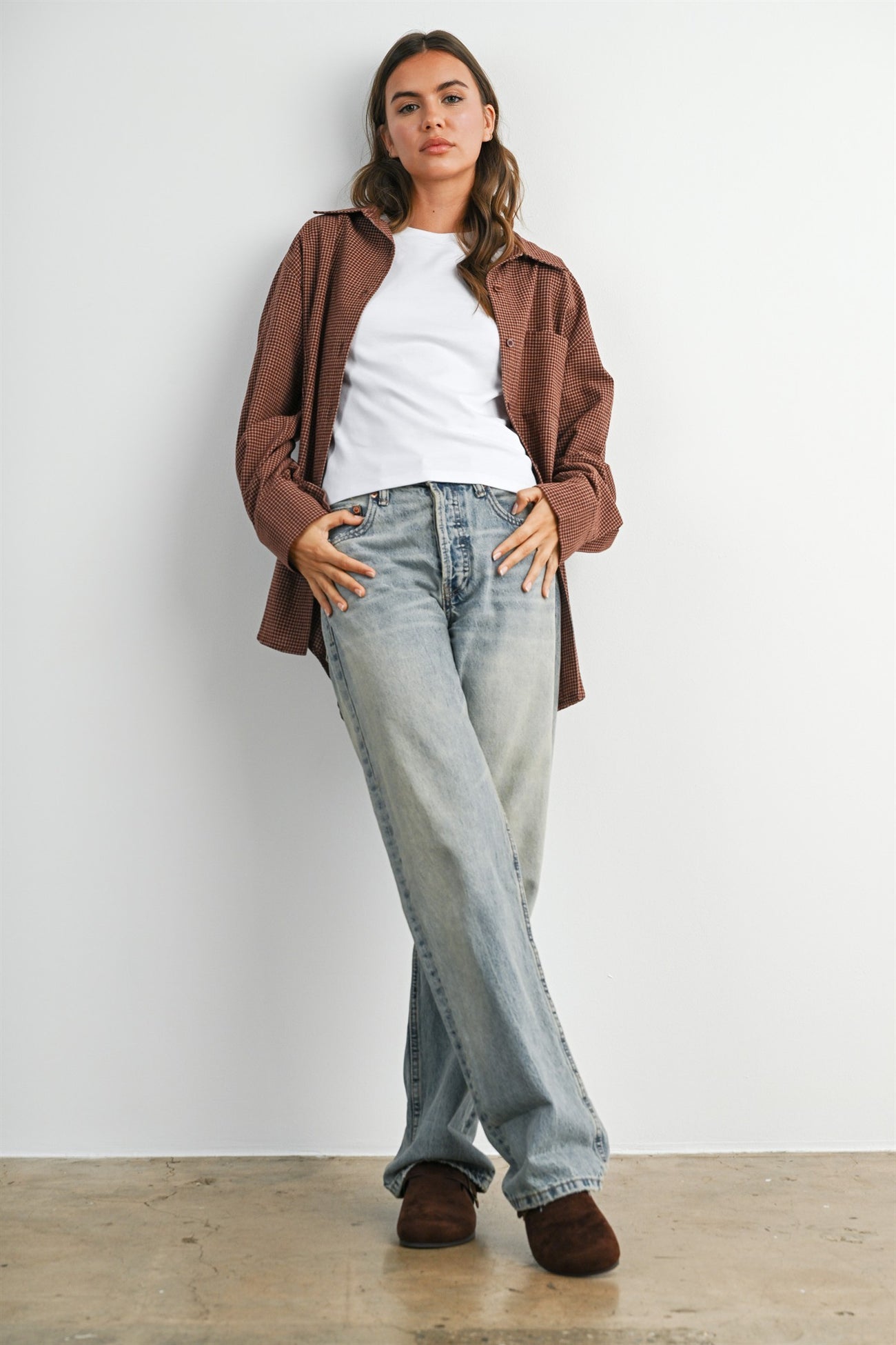 woman wearing a brown button-up shirt over a white t-shirt and light blue wide-leg jeans with brown slippers