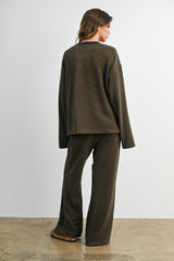 woman wearing a dark olive green long sleeve top and matching wide-leg pants, viewed from the back