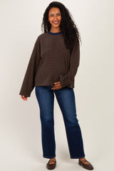 woman wearing a dark brown maternity top with long sleeves and blue trim, paired with blue straight leg jeans and smiling